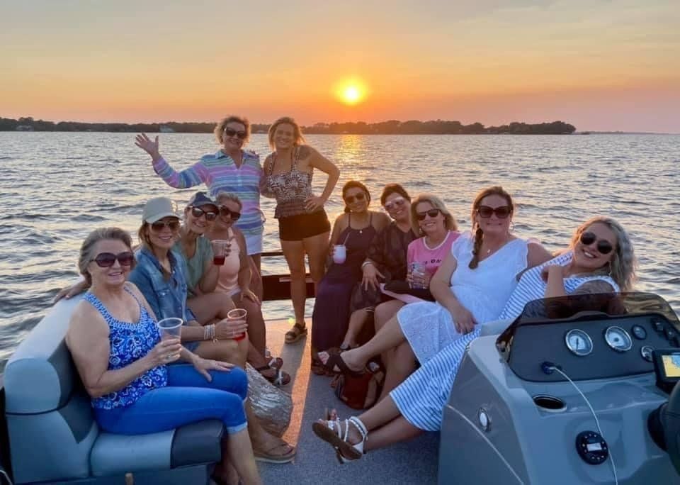 A group of women are sitting on a boat in the water at sunset.