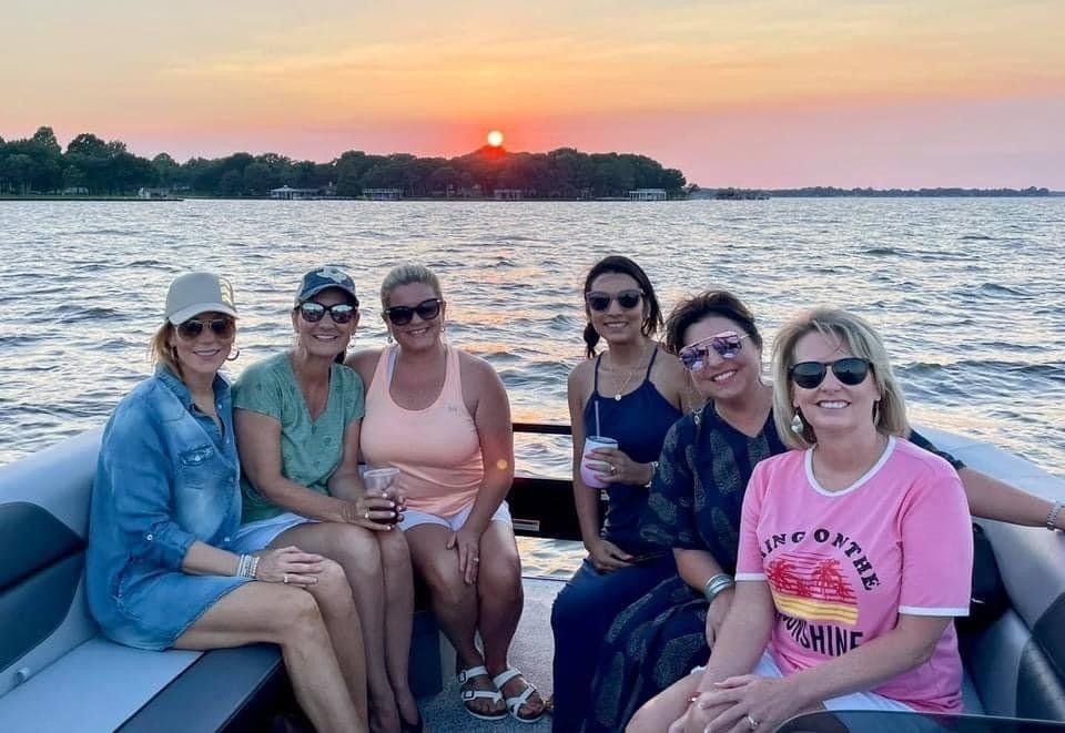 A group of women are sitting on a boat in the water at sunset.