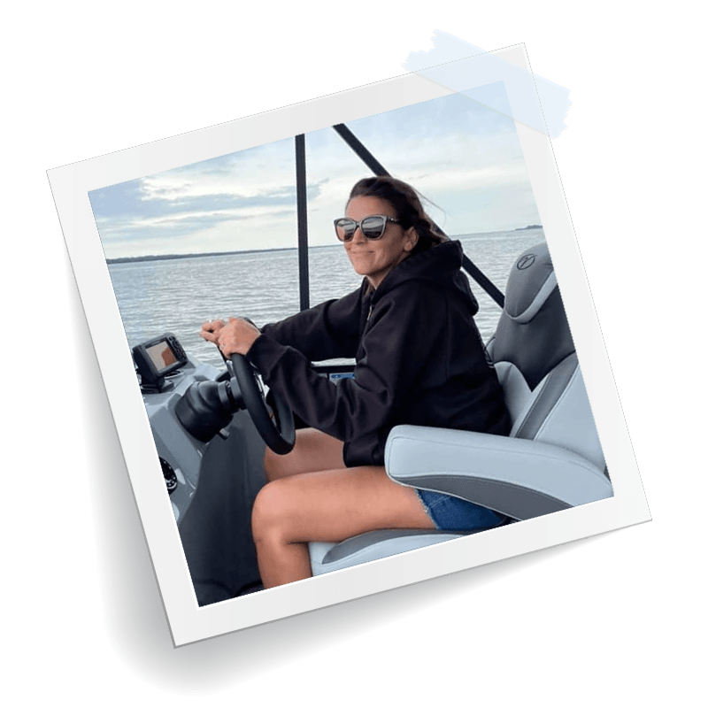 A woman is sitting at the steering wheel of a boat.