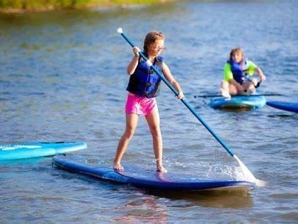 A young girl is standing on a paddle board in the water.