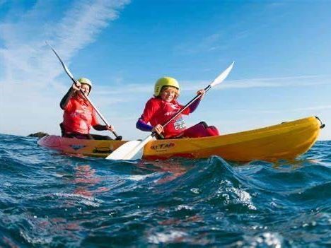 Two people are paddling kayaks in the ocean.