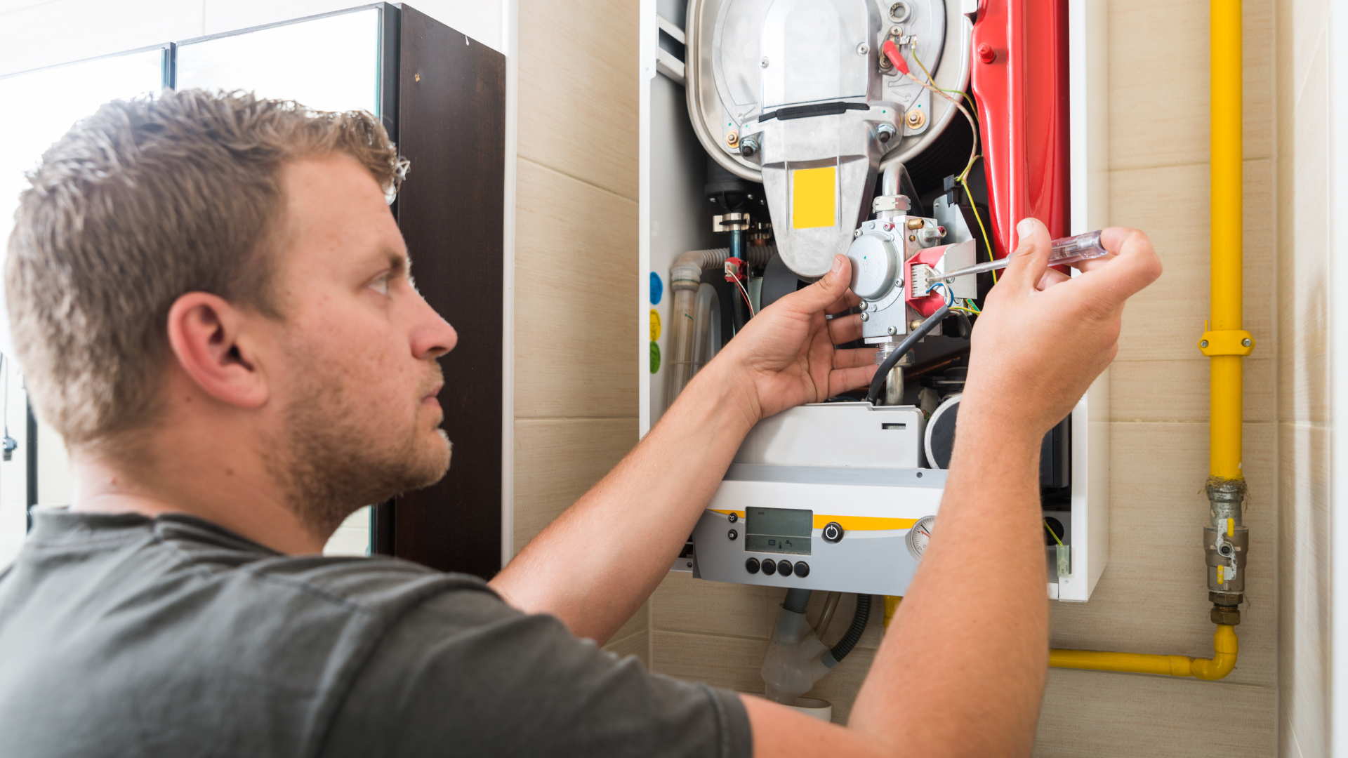 A man is fixing a boiler with a screwdriver.
