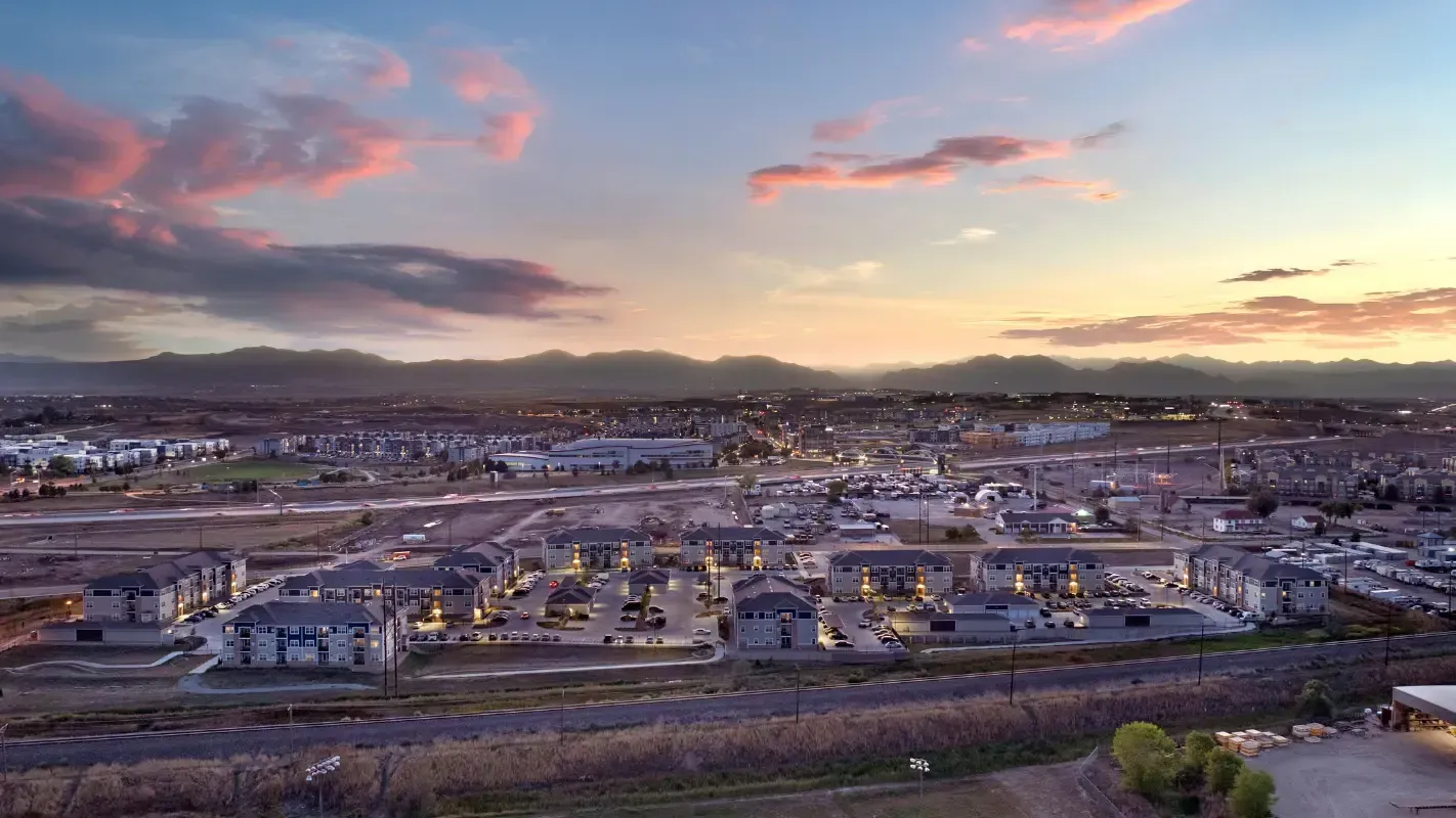 Aerial view of a large apartment community with multiple buildings and parking lots at sunset.