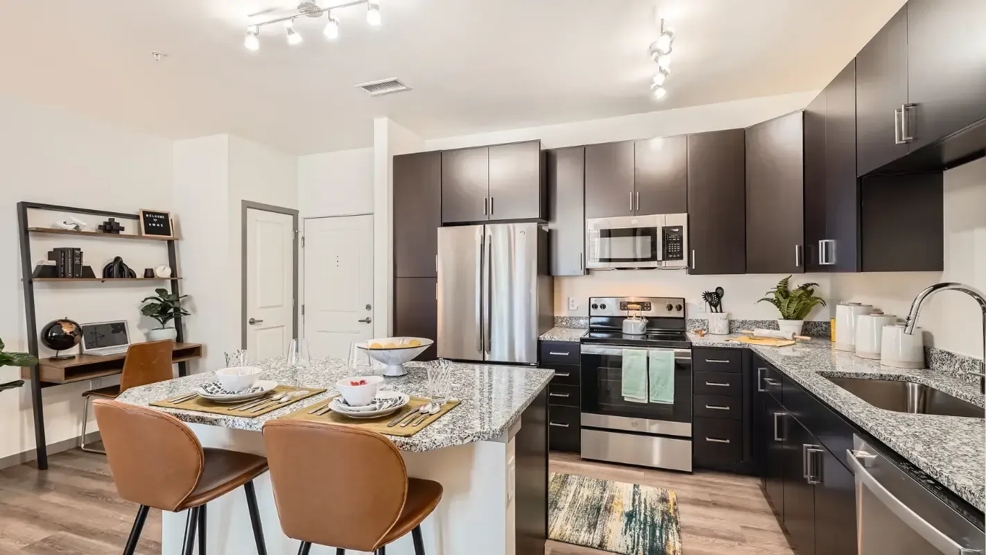Modern kitchen in a contemporary apartment with dark cabinets, stainless steel appliances, granite countertops, and an island with seating.