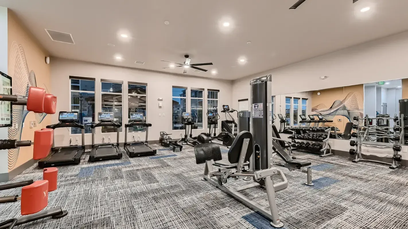 Modern resident fitness center with treadmills, weight machines, and free weights, bright with mirrors.