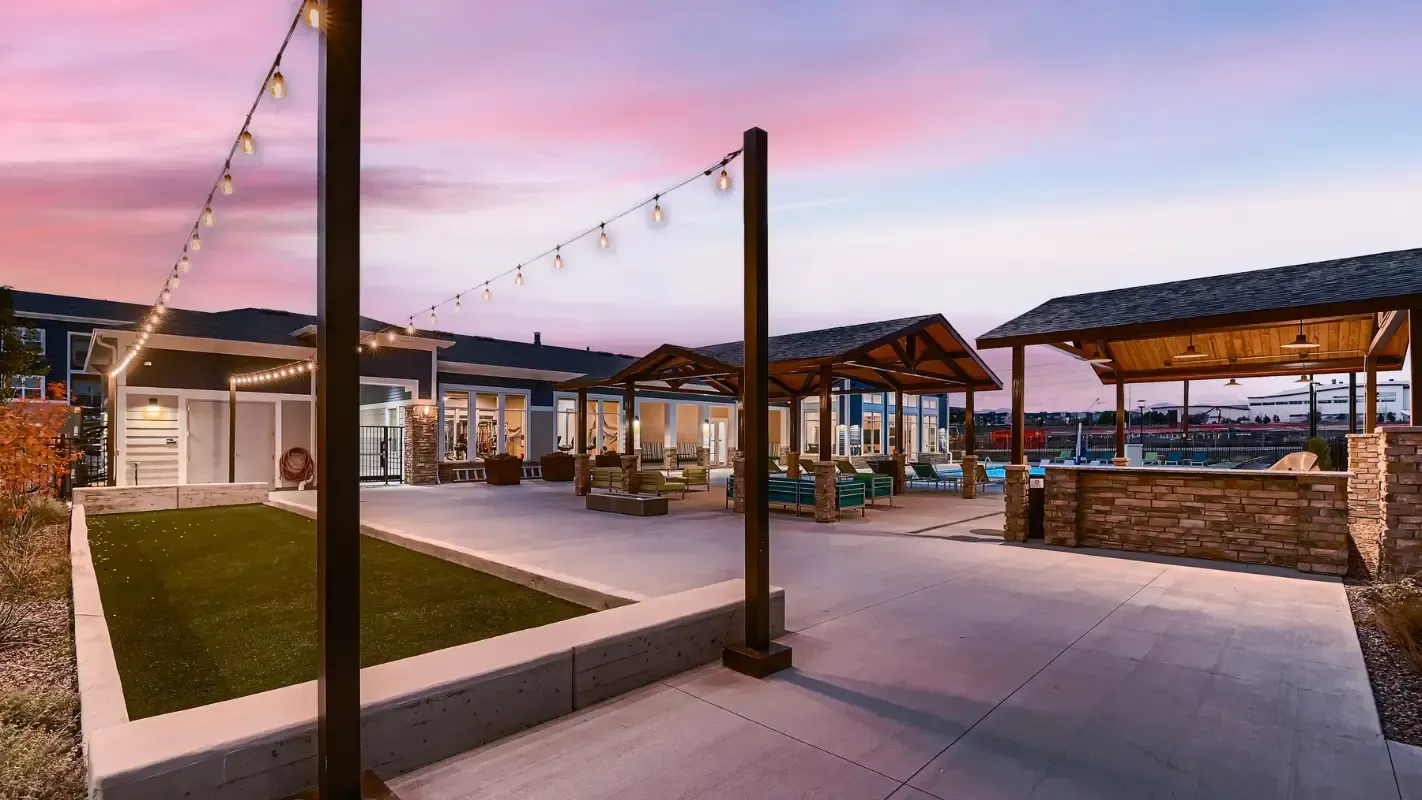 Outdoor community courtyard at dusk with string lights, seating areas, and covered pavilions.