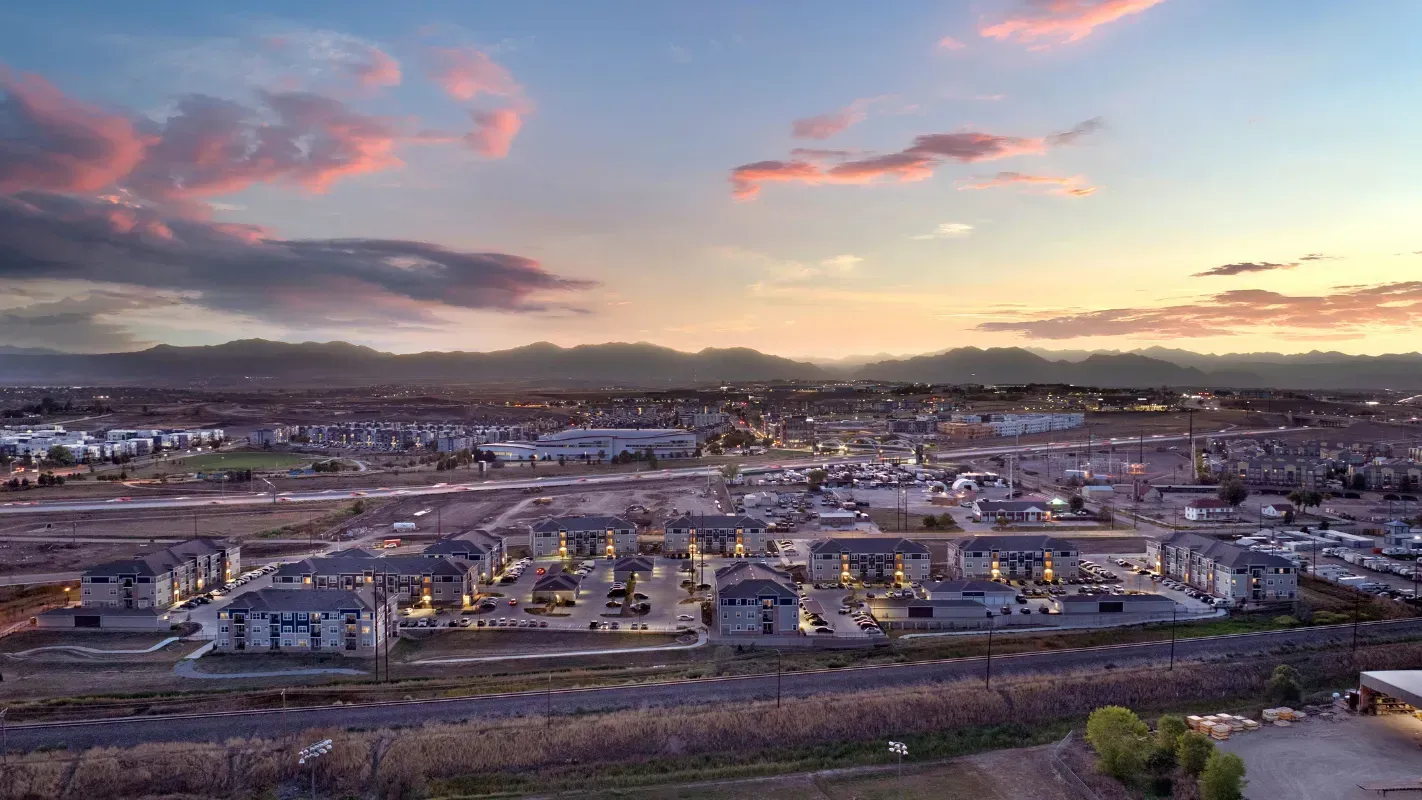 Aerial view of a multifamily community with rows of buildings and parking at sunset.