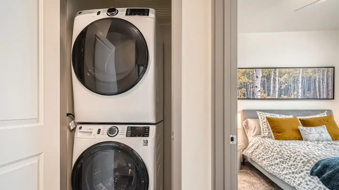 Stacked washer and dryer in a small closet beside a bedroom.