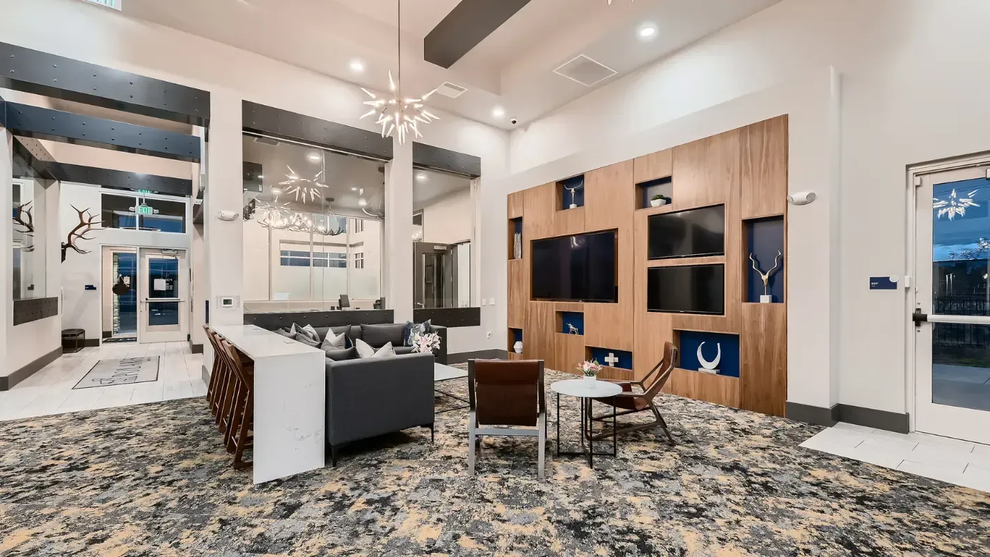 Modern apartment lobby with seating, a wood media wall, and glass entry doors.