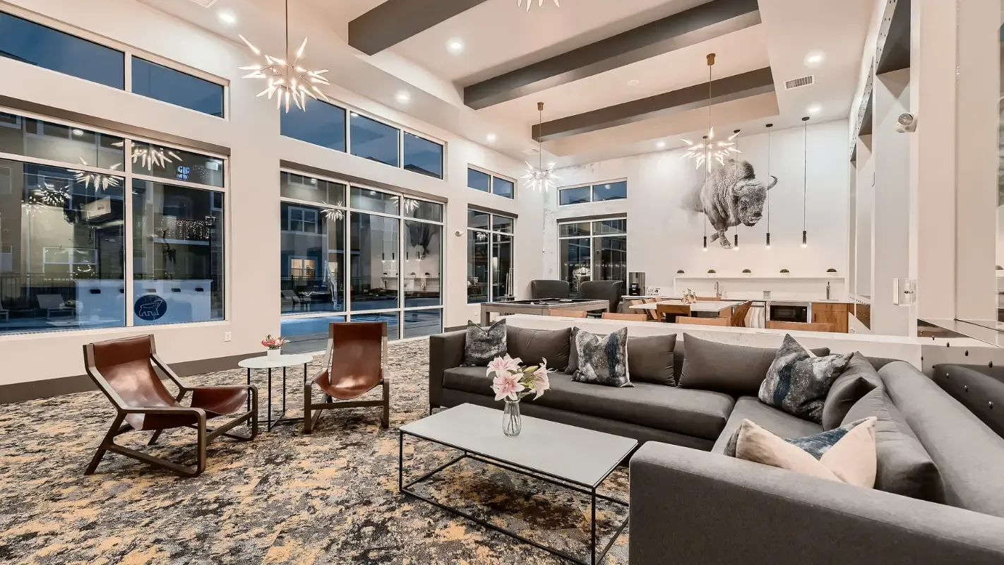 Bright, open resident lounge with comfortable seating, large windows, and a kitchenette.