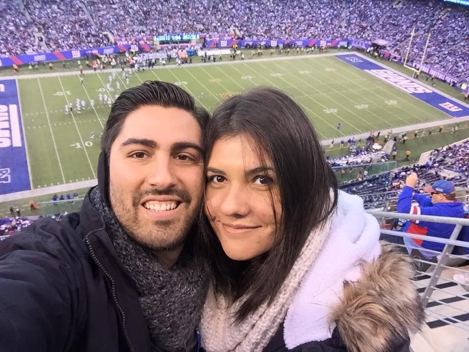 A man and a woman are posing for a picture at a football game.
