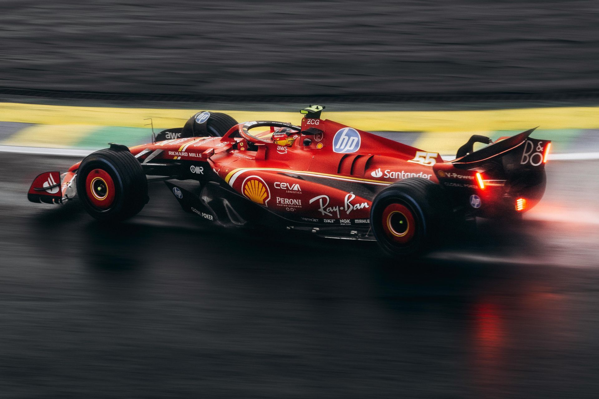 A red race car is driving down a wet track.