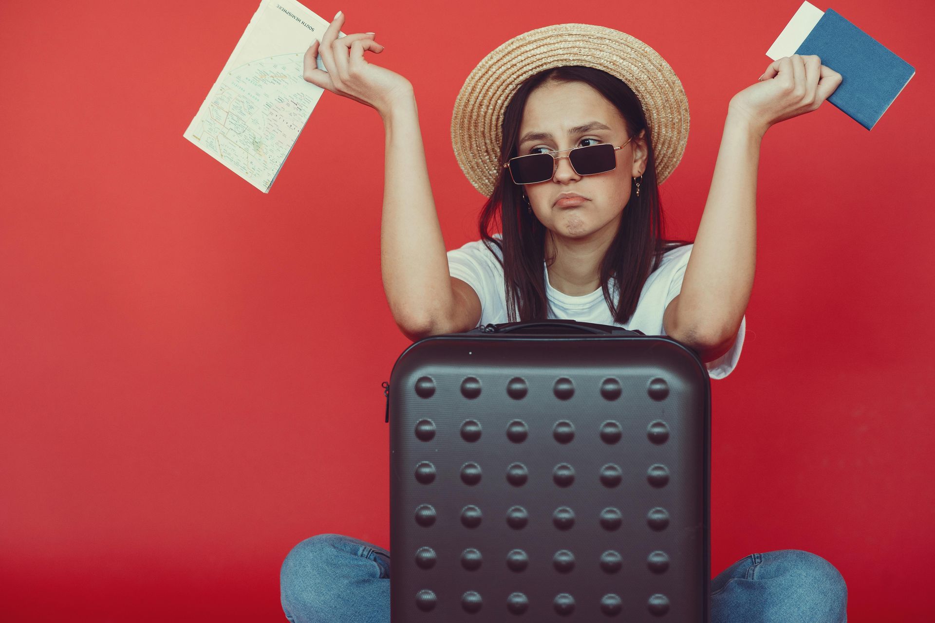 A woman is sitting next to a suitcase holding a passport and a ticket.