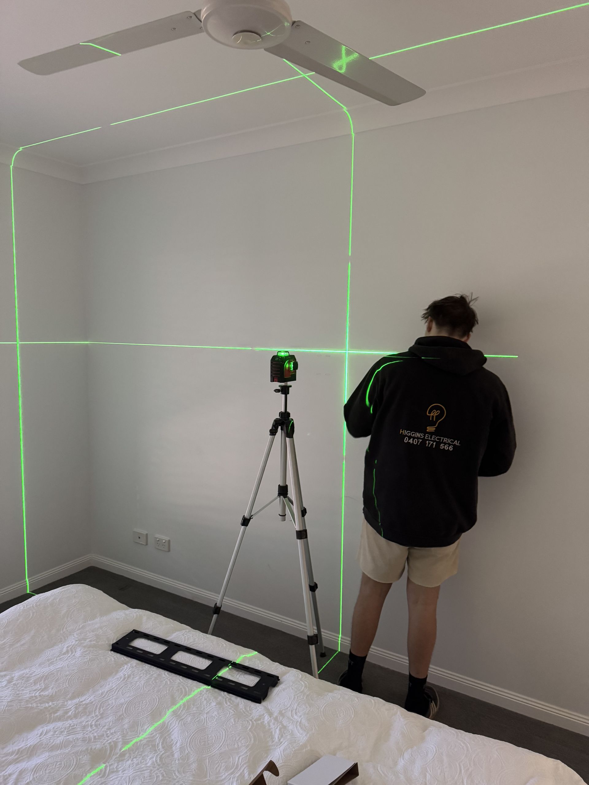 Person using a green laser level on a tripod in a white room, checking a wall — Higgins Electrical in Beerwah, QLD