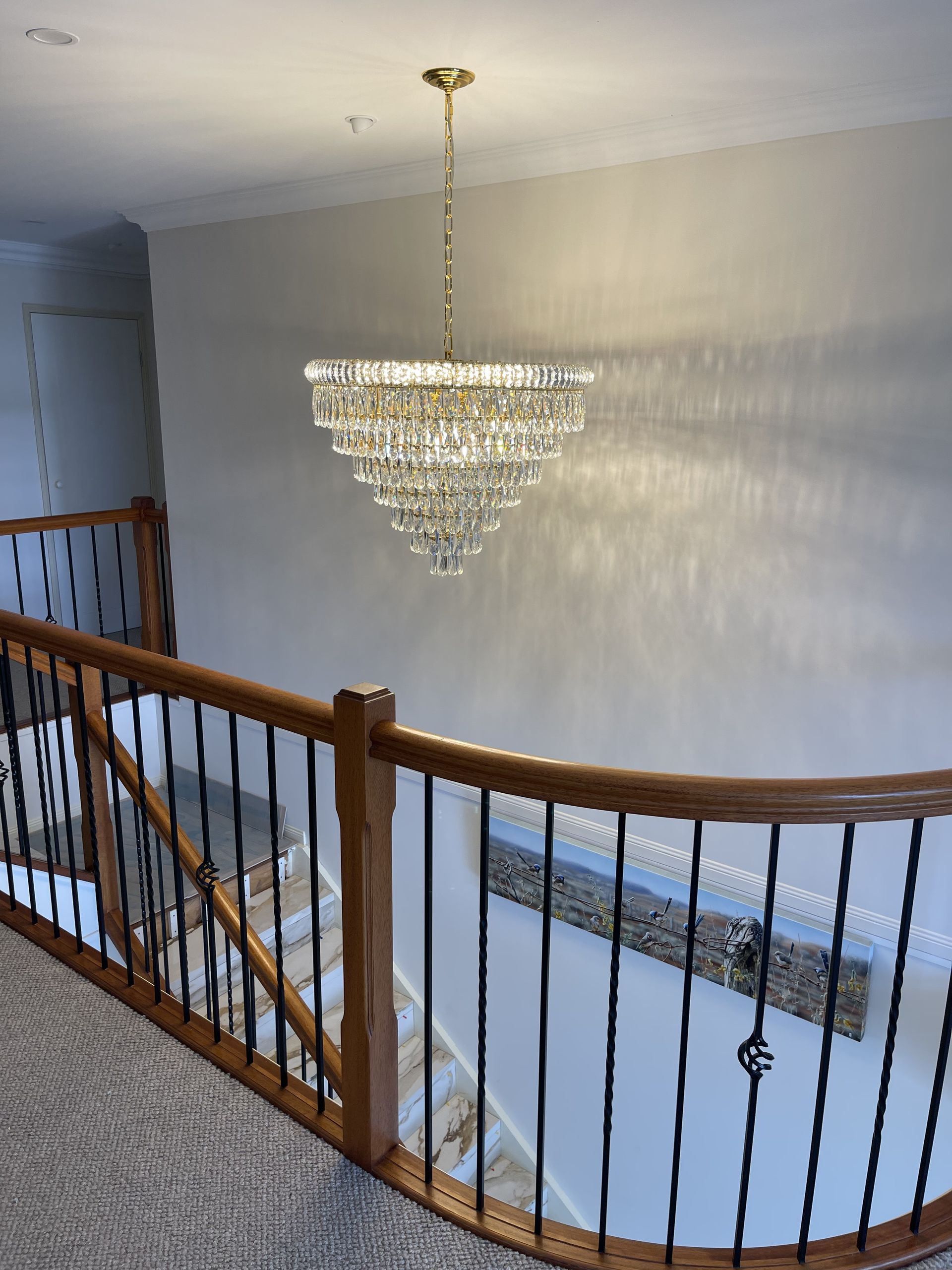 A chandelier hangs above a staircase with wood railing and black spindles — Higgins Electrical in Beerwah, QLD