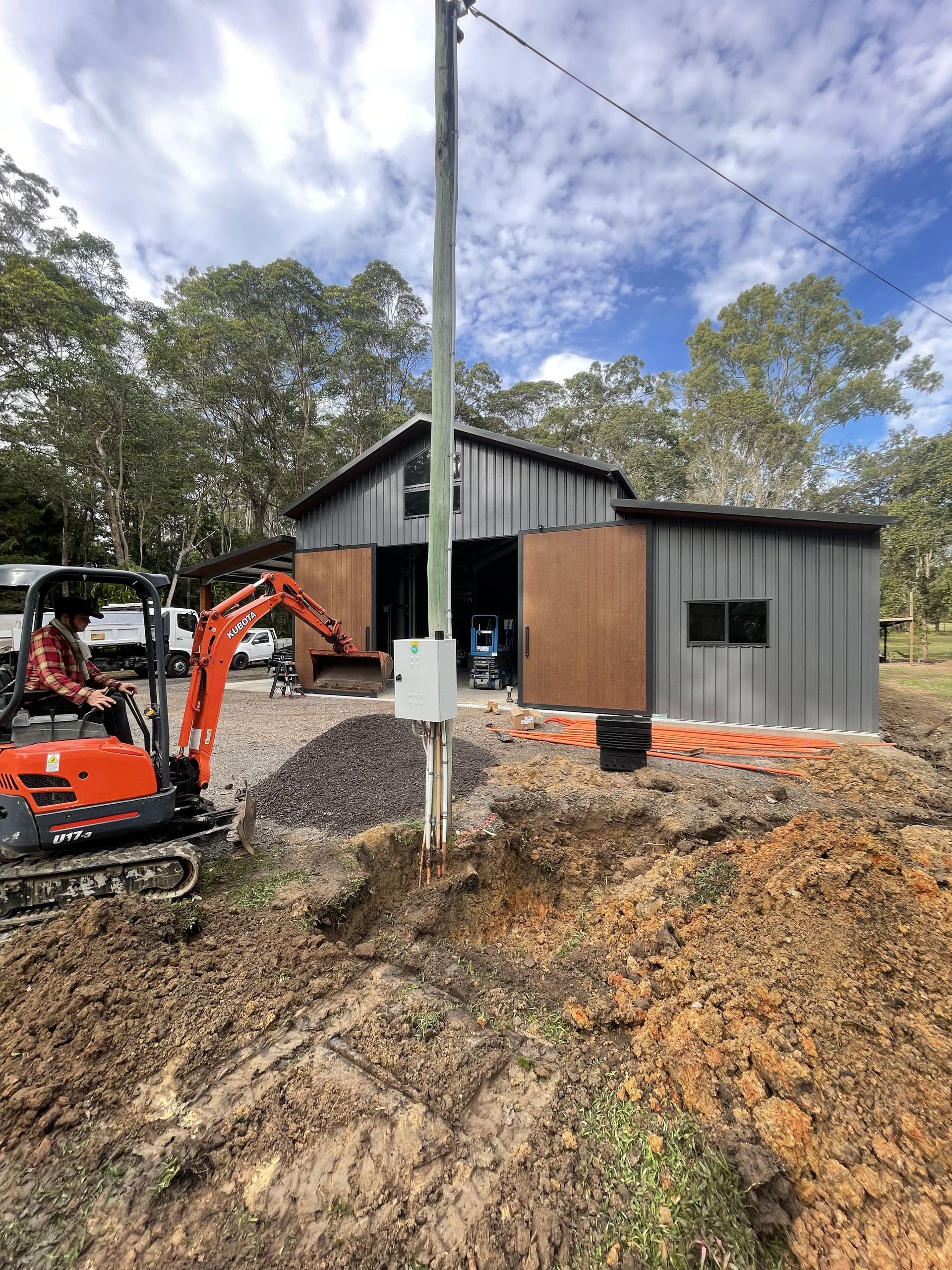 Construction site with mini excavator; a partially built metal shed, utility pole — Higgins Electrical in Beerwah, QLD