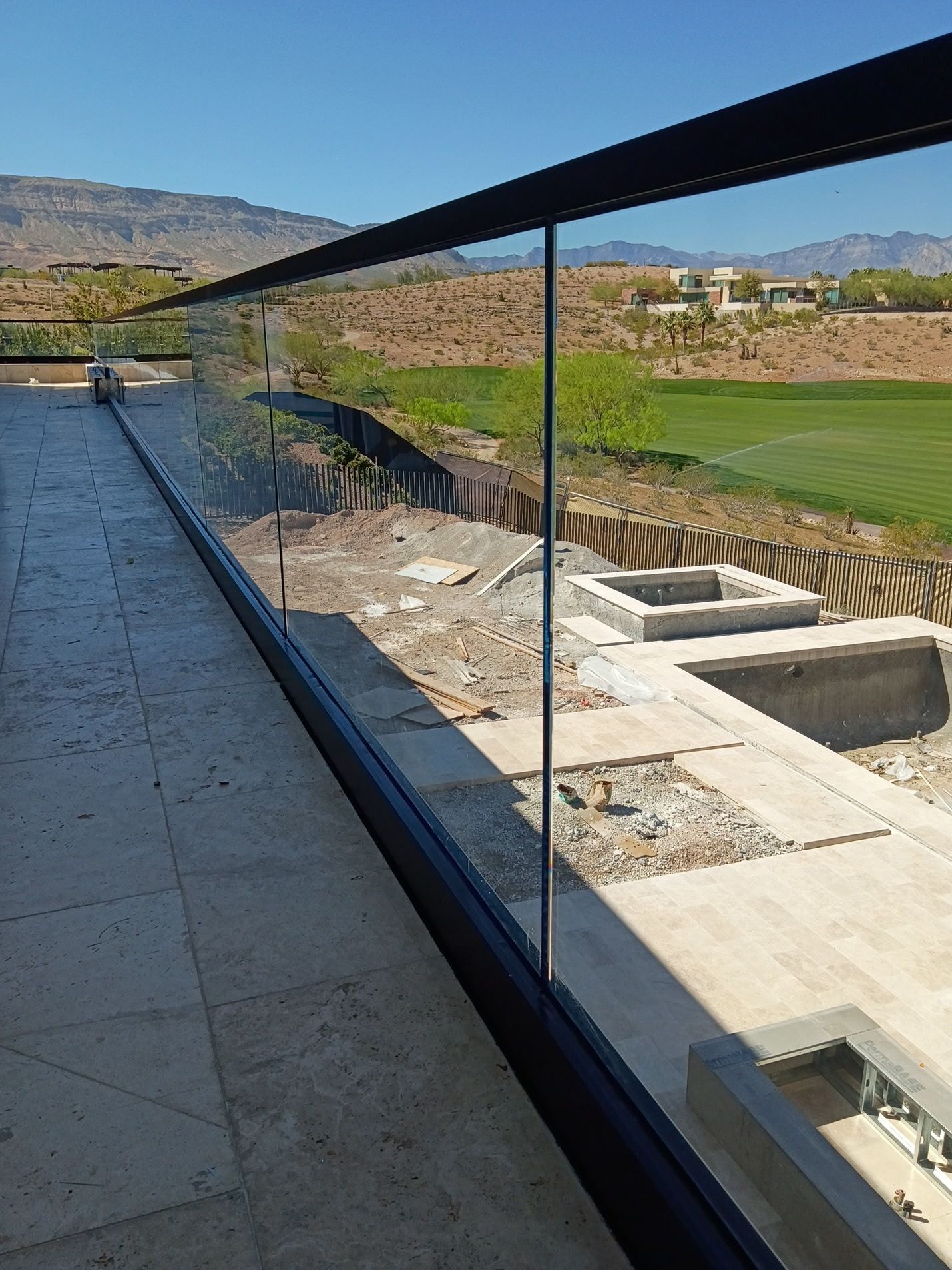 A modern terrace with a glass and black metal railing overlooking a landscape with a grassy area and distant mountains.