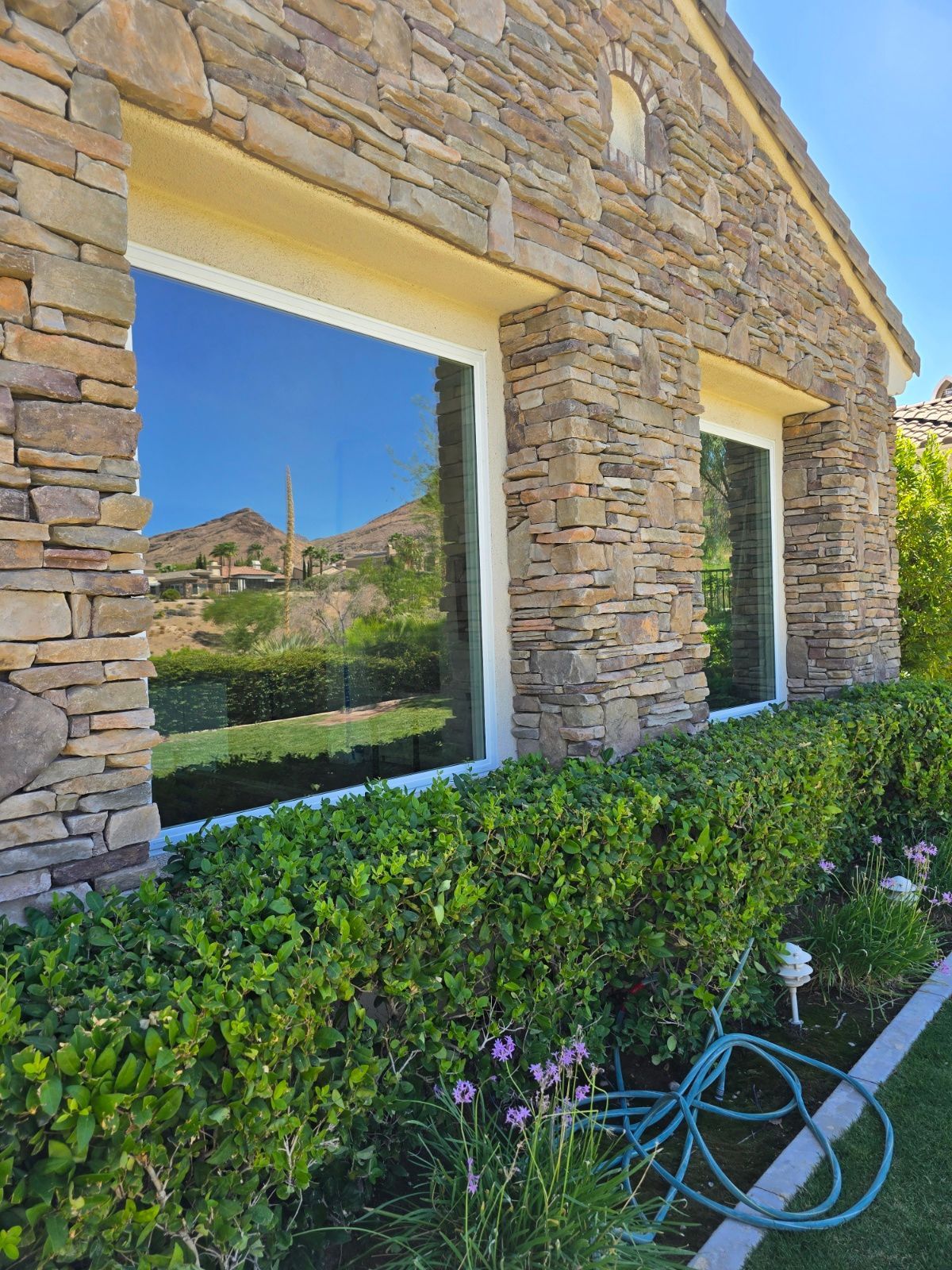 A stone building with two windows and a hose in front of it.