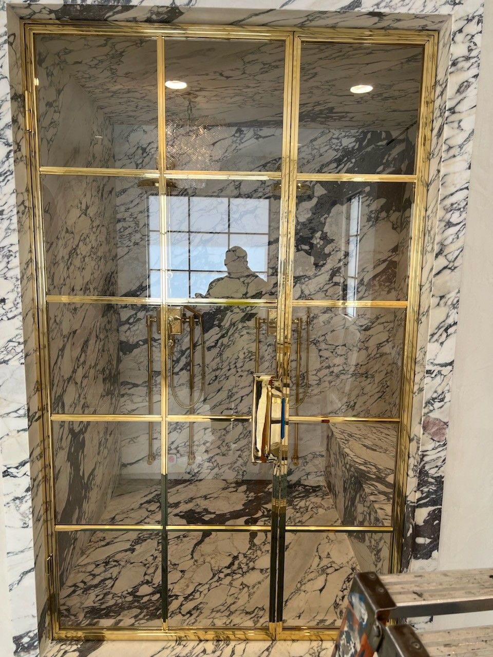 A bathroom with marble walls and a glass door with gold trim.