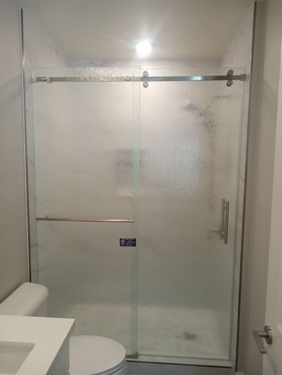 A bathroom with a toilet , sink and shower with a sliding glass door.