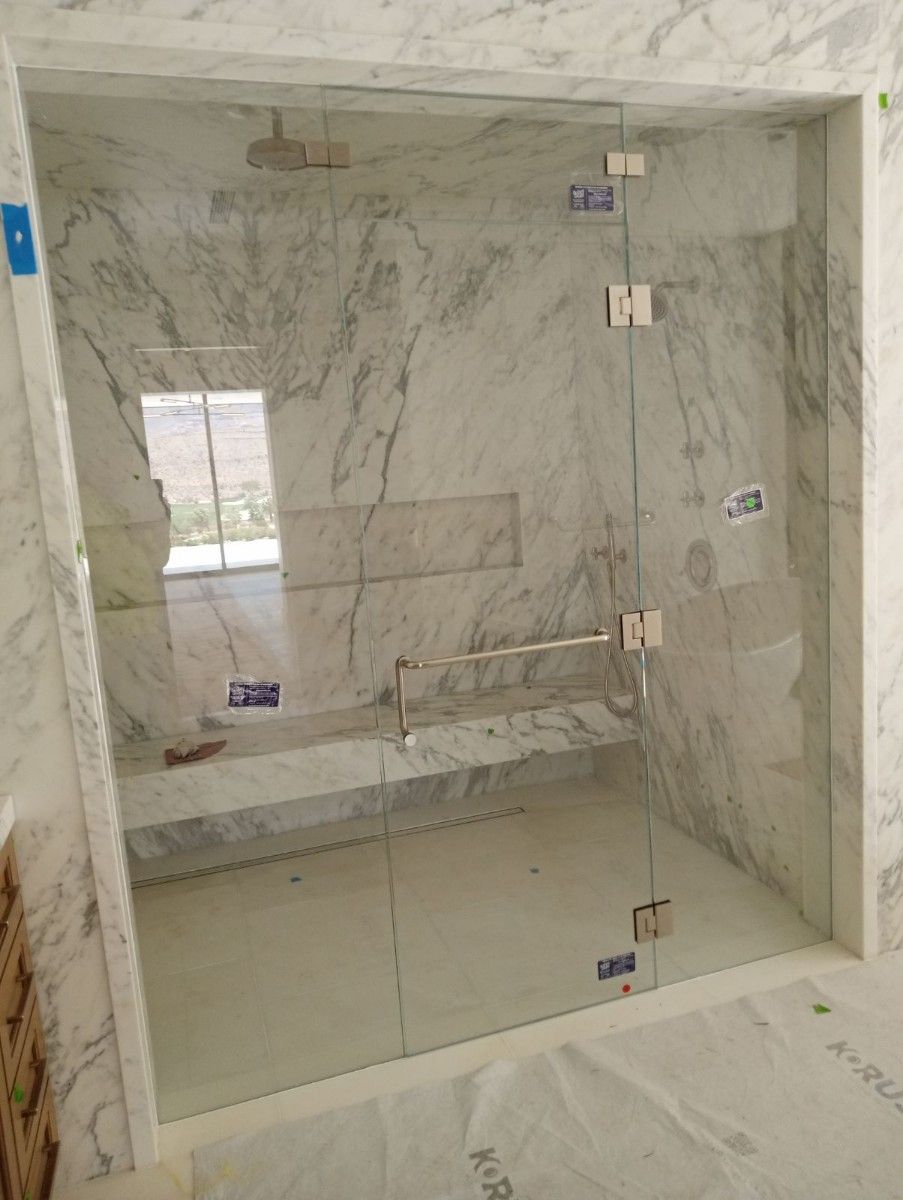 A bathroom with marble walls and a glass shower door.