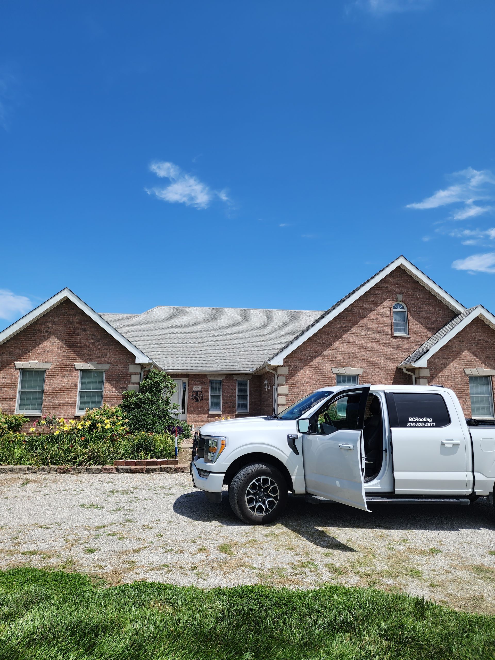 A white truck is parked in front of a brick house.