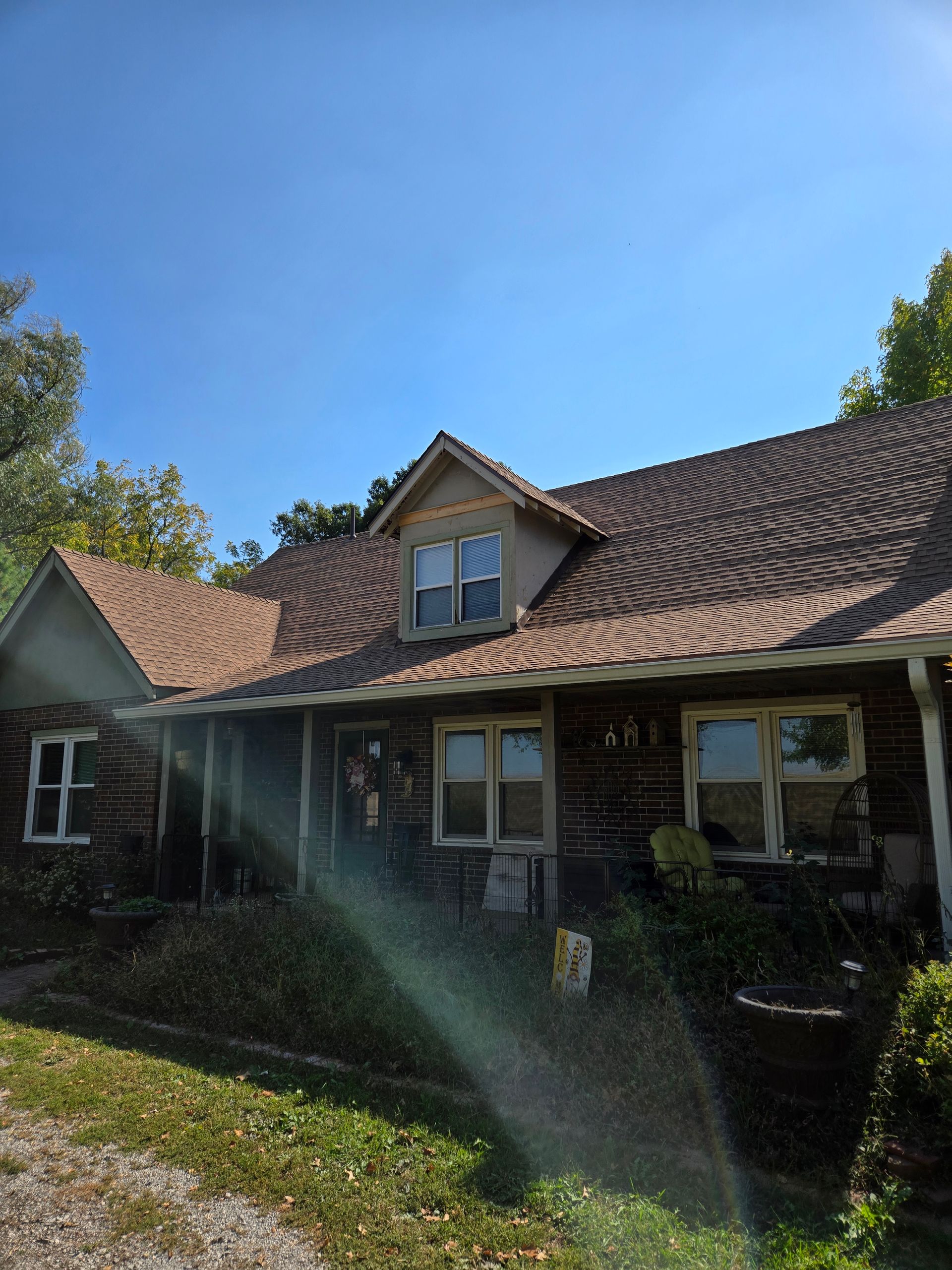 A house with a brown roof and a porch on a sunny day.
