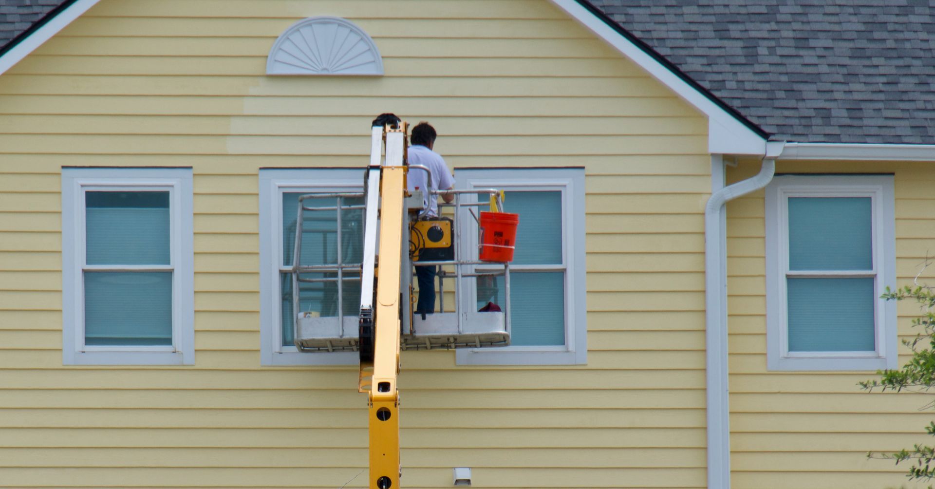 A man is painting a window on the side of a house.