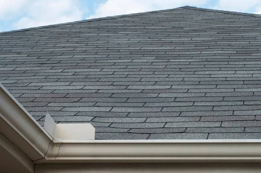 A close up of a roof with shingles and a white gutter.