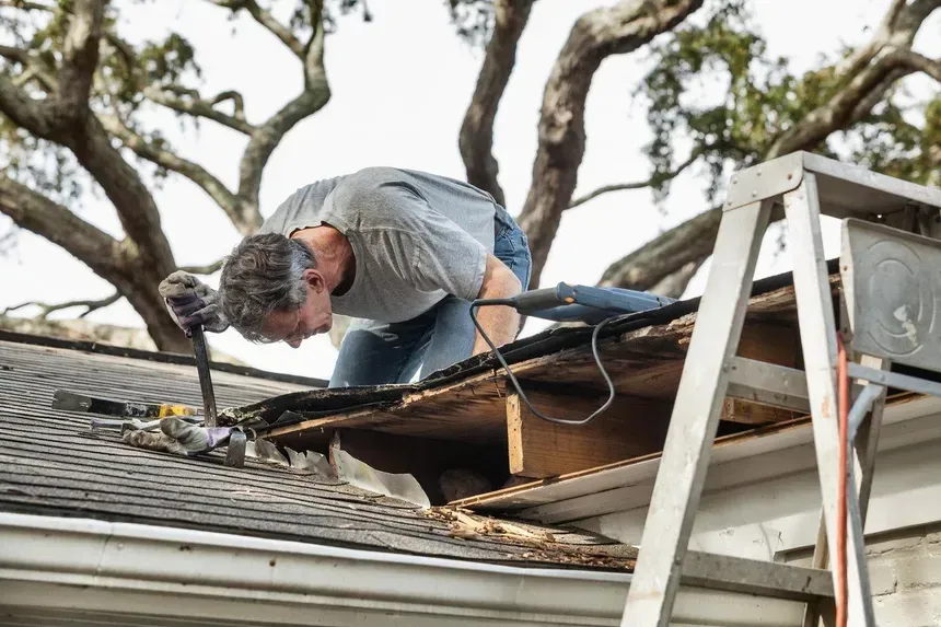 A man is working on the roof of a house with a hammer.