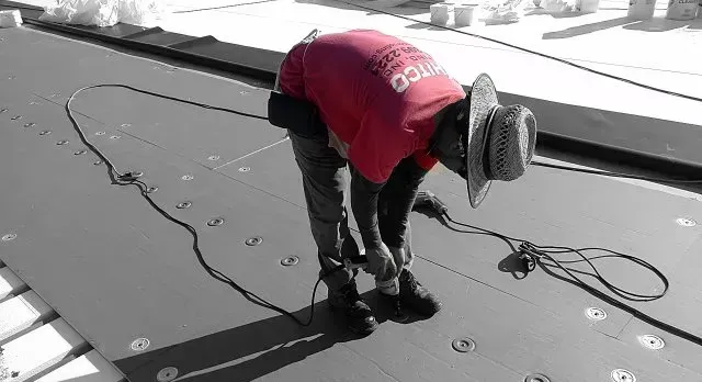 A man wearing a red shirt and a hat is working on a roof.