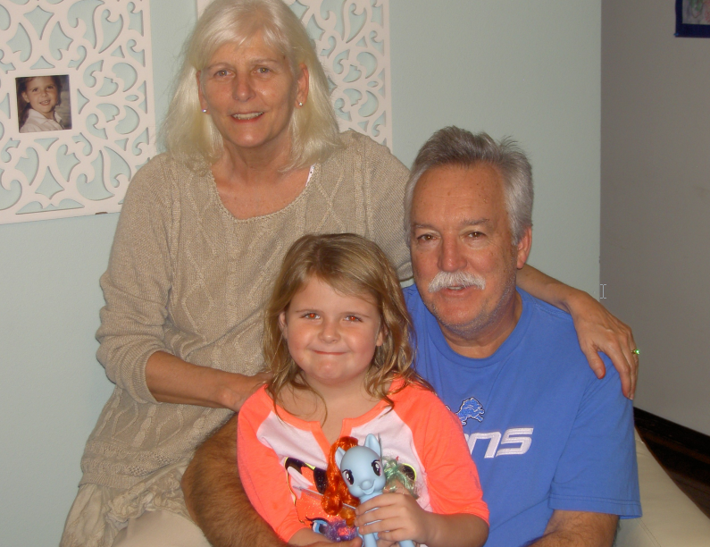 A man and woman are posing for a picture with a little girl who is holding a stuffed animal.