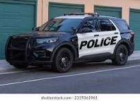 A black and white police car is parked on the side of the road in front of a garage.