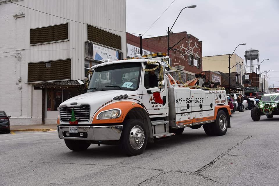 White and orange tow truck driving down a street lined with buildings and a water tower.