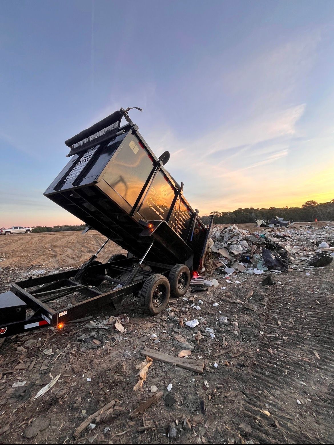 Dump trailer dumping trash at a landfill during dusk.