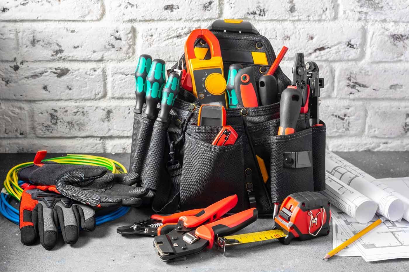 A tool bag filled with electrical tools and gloves on a table.