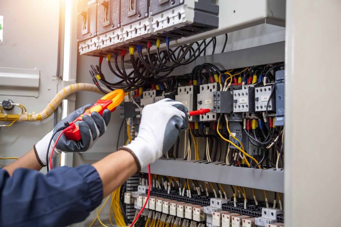 An electrician is working on an electrical box with a multimeter.