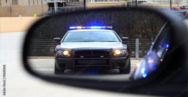 A police car is reflected in the rear view mirror of a car.