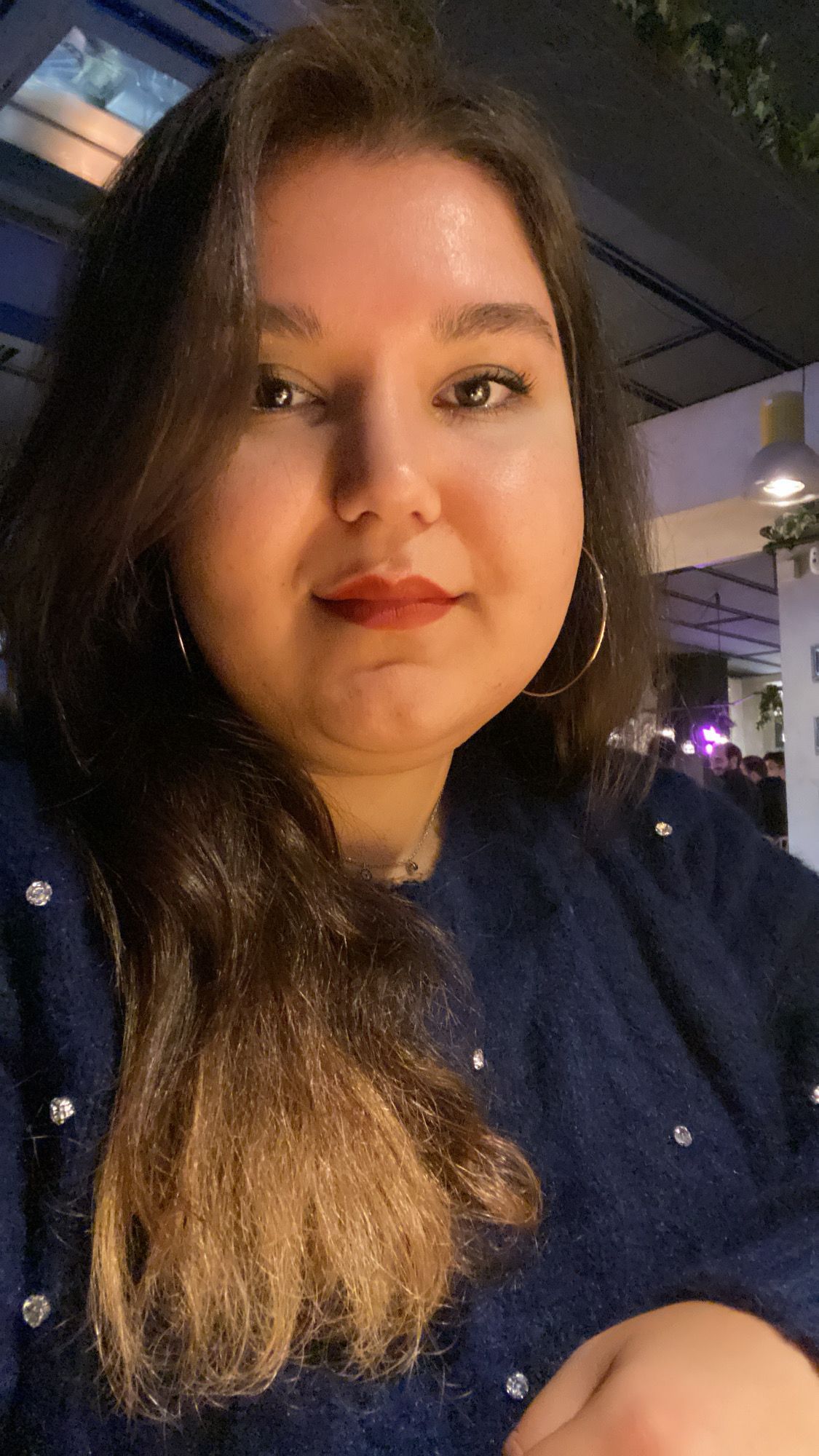 Uma mulher vestindo um suéter azul e brincos de argola está tirando uma selfie.