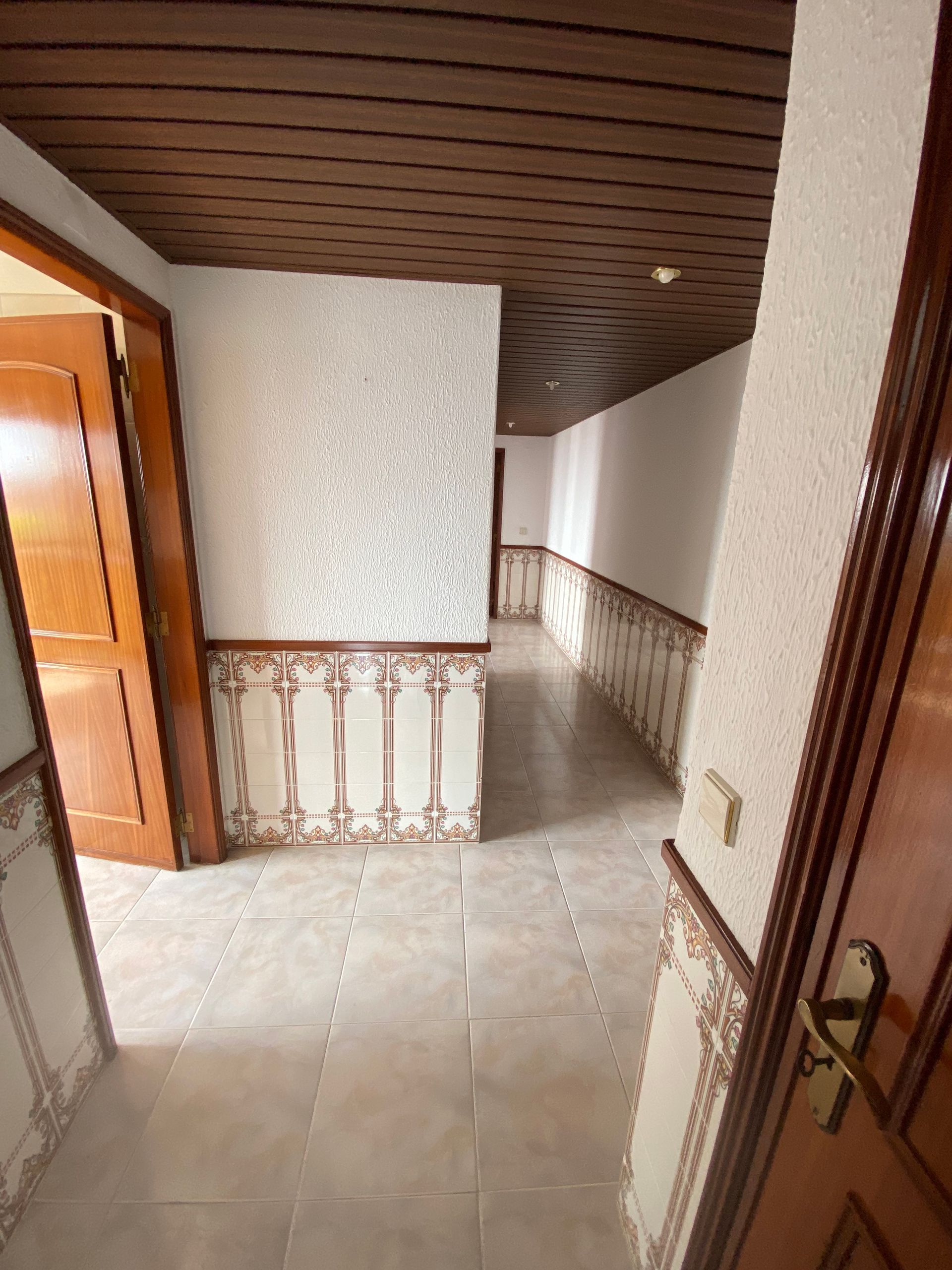 Um longo corredor com teto de madeira e piso de cerâmica