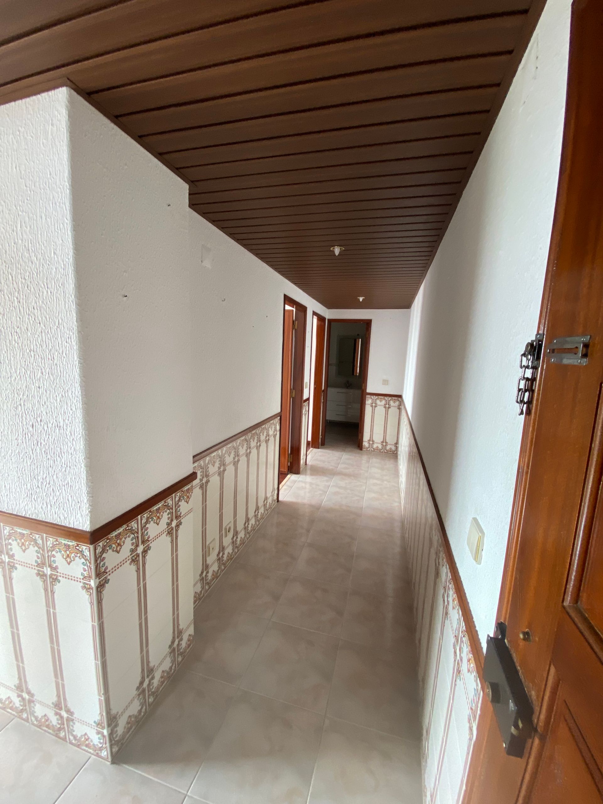 Um longo corredor com teto de madeira e uma porta