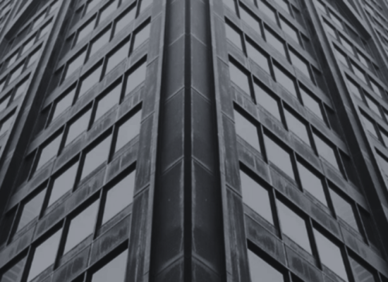 Low-angle view of a gray, multi-story office building corner with repeating windows.