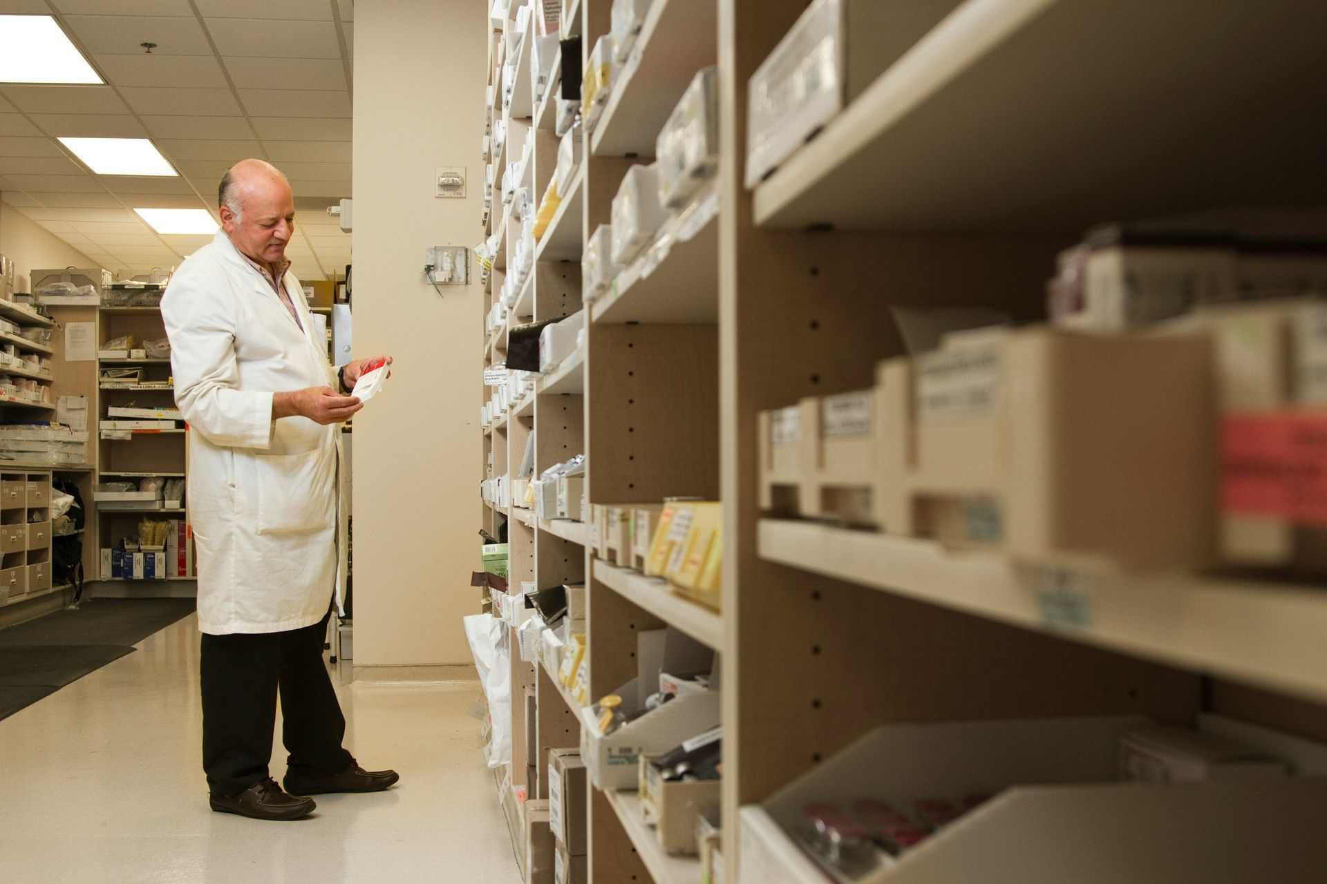 A man in a lab coat is looking at a bottle in a pharmacy.