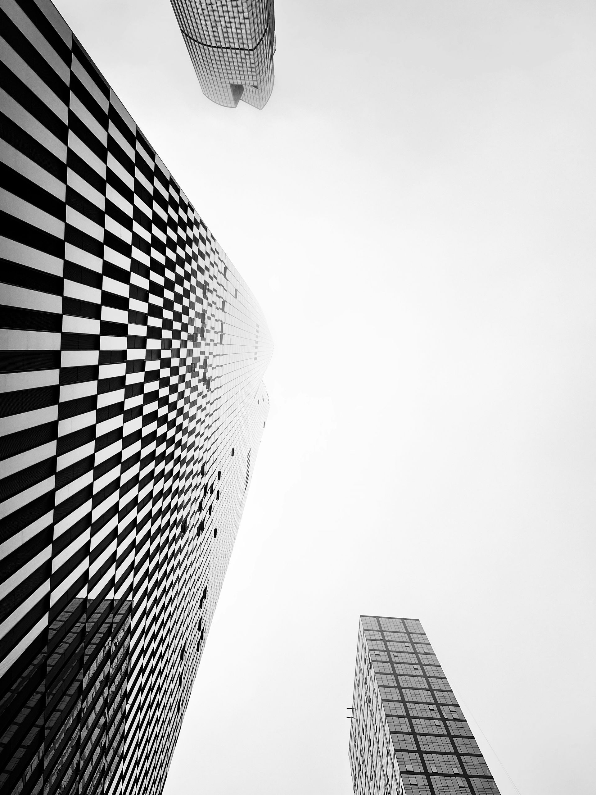 Black and white photo of three high-rise buildings angled upwards; checkered facade dominates.