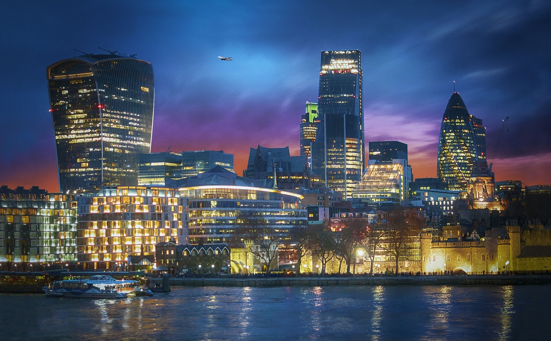 City skyline at dusk with illuminated modern towers reflecting on the water.