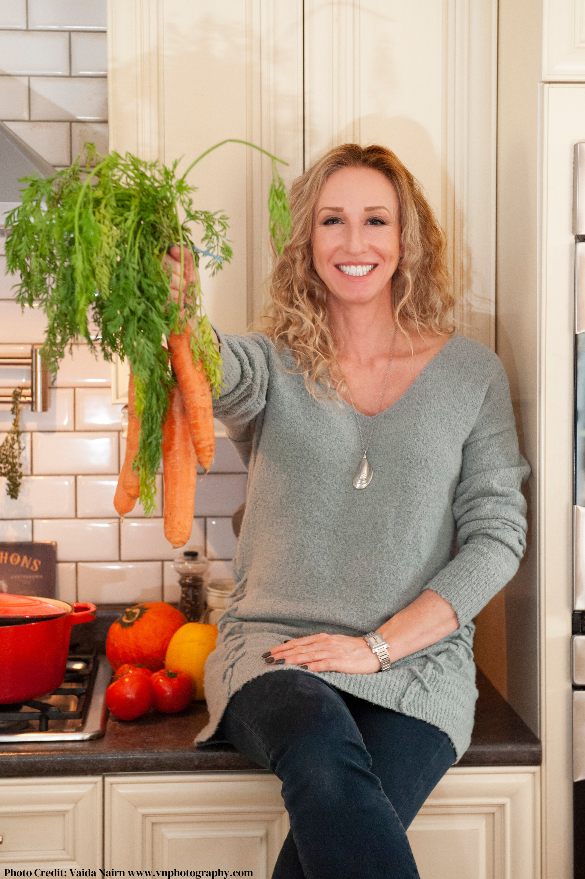 Woman holding carrots in a kitchen, smiling.