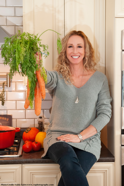Woman holding carrots in a kitchen, smiling.