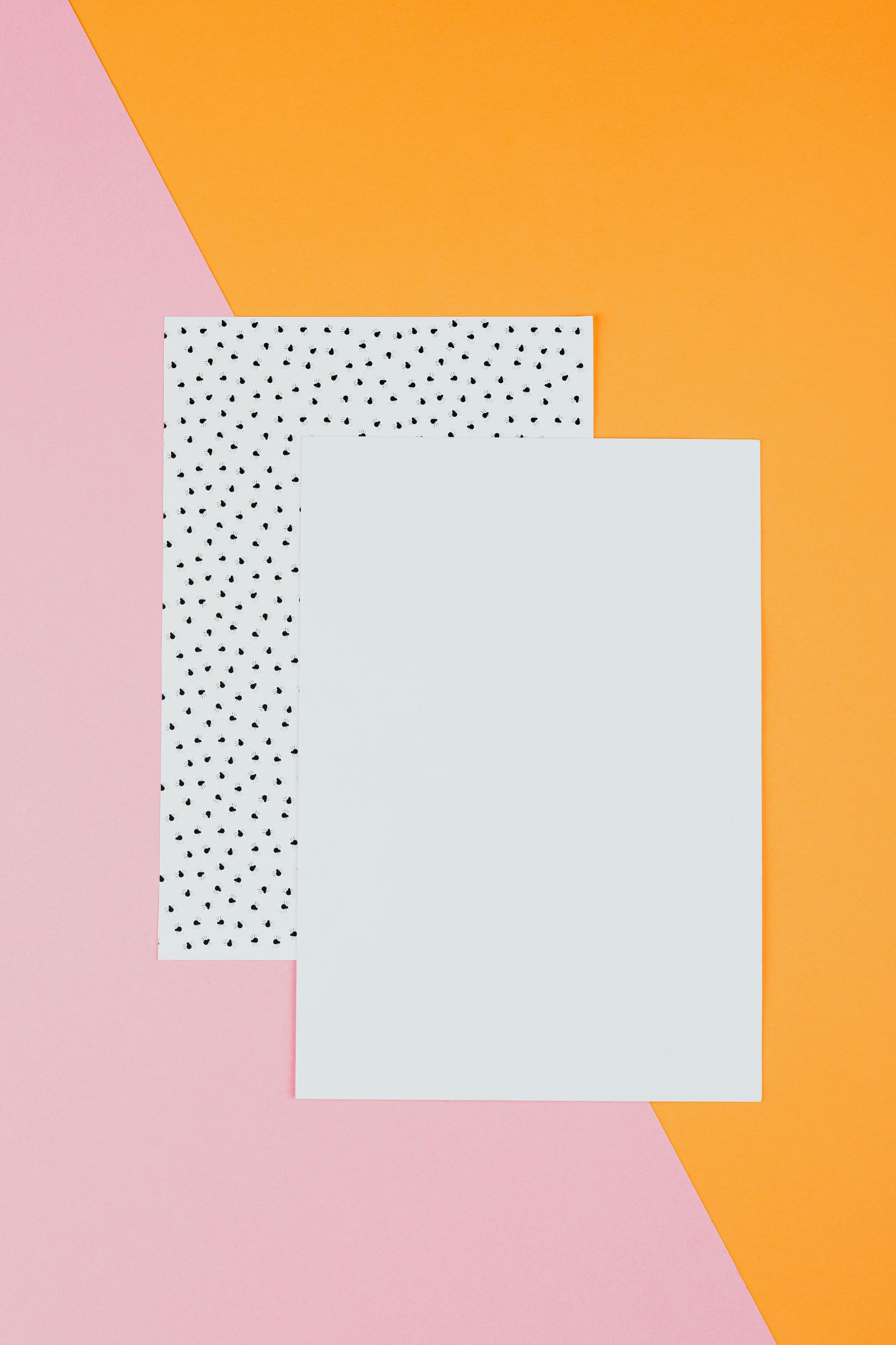 Two pieces of paper are sitting on top of each other on a pink and orange background.