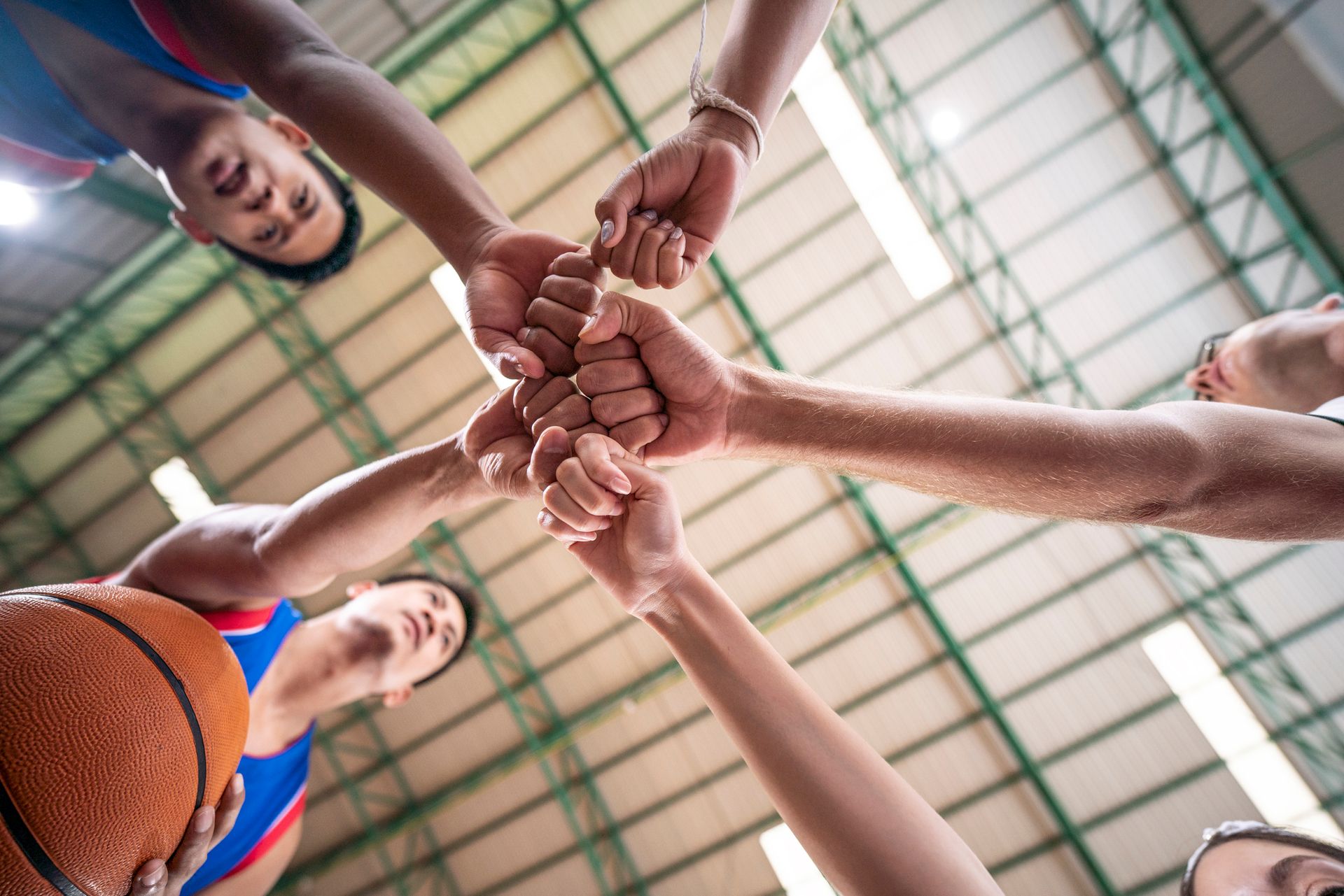 Basketball players huddle, fist-bumping.  They wear blue and white uniforms inside a gymnasium.  A basketball is visible.