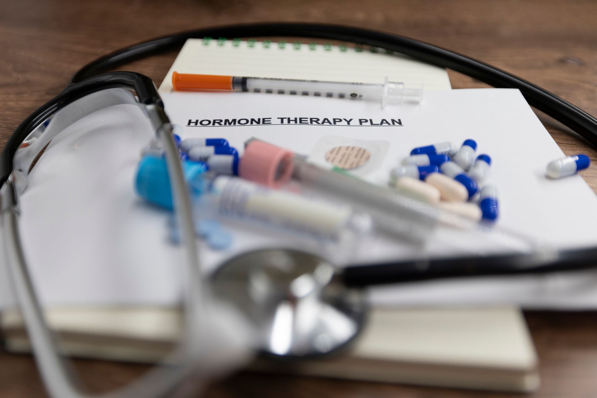 Stethoscope, pills, syringes, and a 'Hormone Therapy Plan' document on a wooden surface.